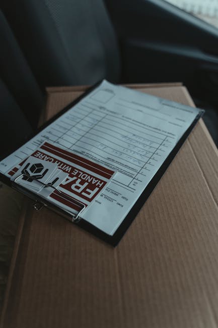 A close-up image showing a flower delivery order form, placed on top of a brown cardboard box inside a vehicle. The form, prominently displaying the red and black 'FRAGILE HANDLE WITH CARE' warning, c